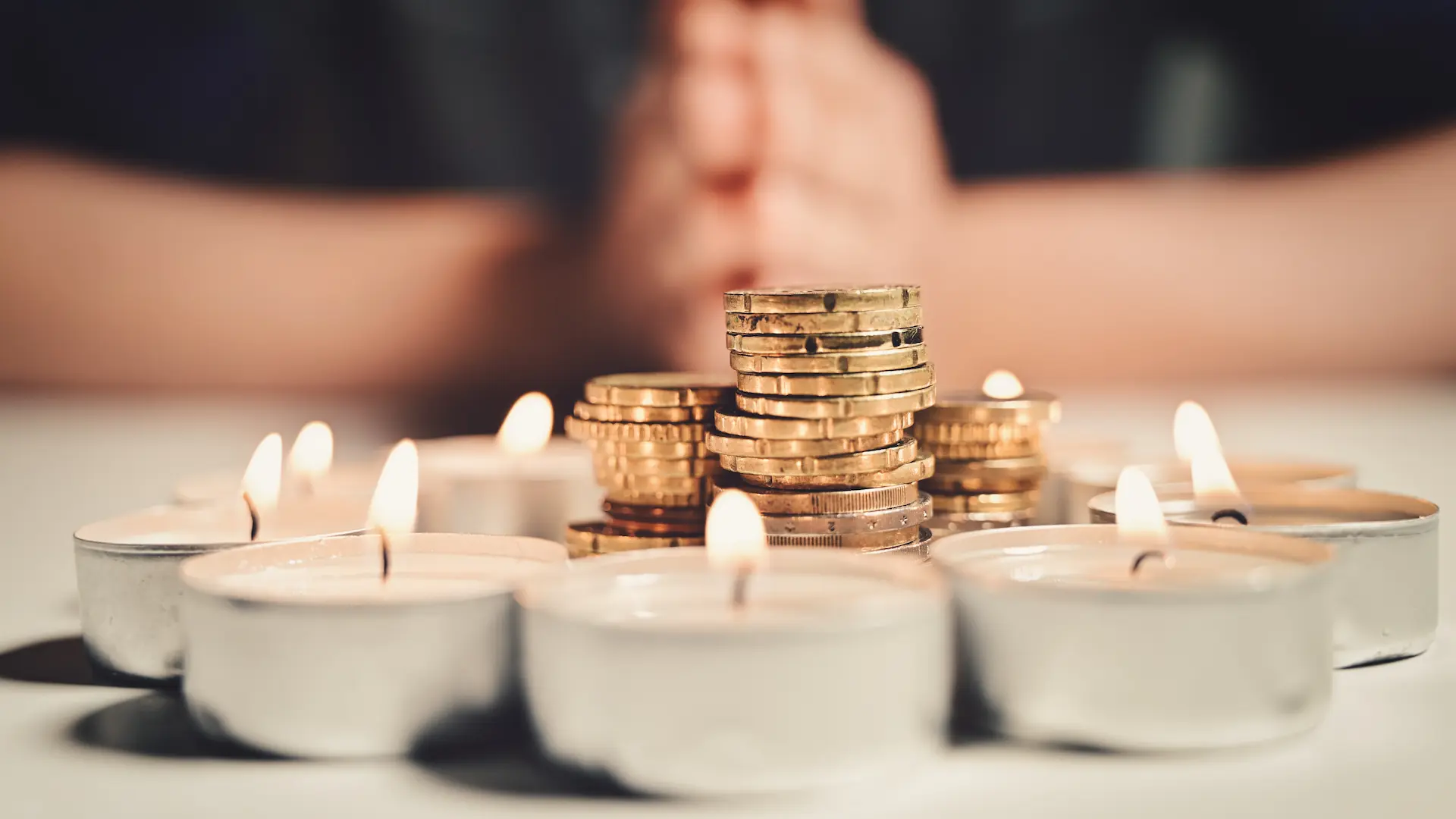 hands-man-praying-with-circle-burning-candles-with-stack-coins-inside